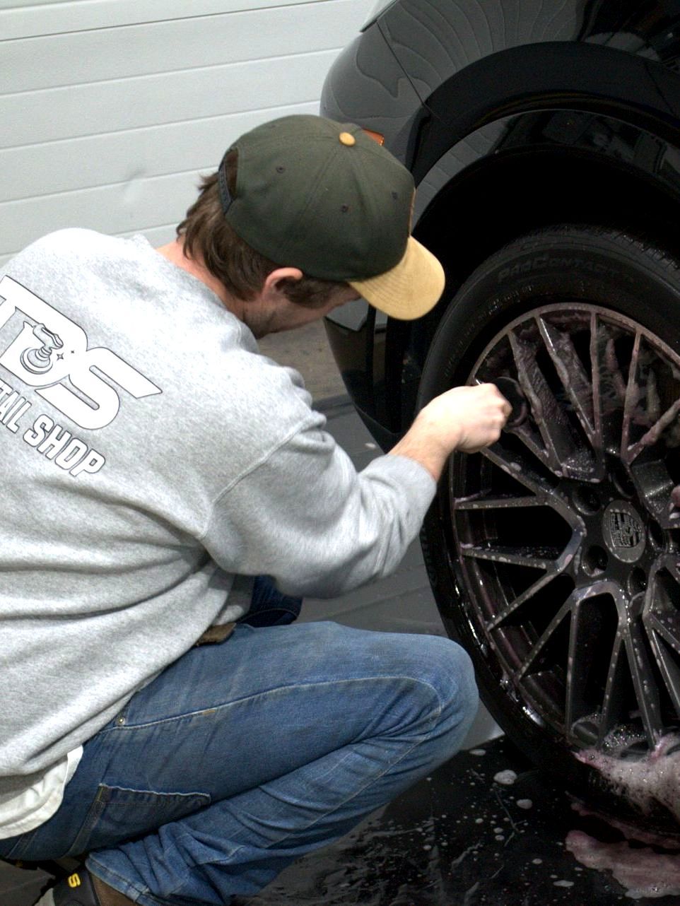 A man is washing a car with foam in a garage.
