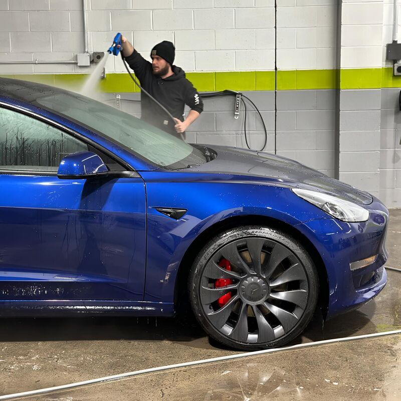 A man is washing a blue car in a garage