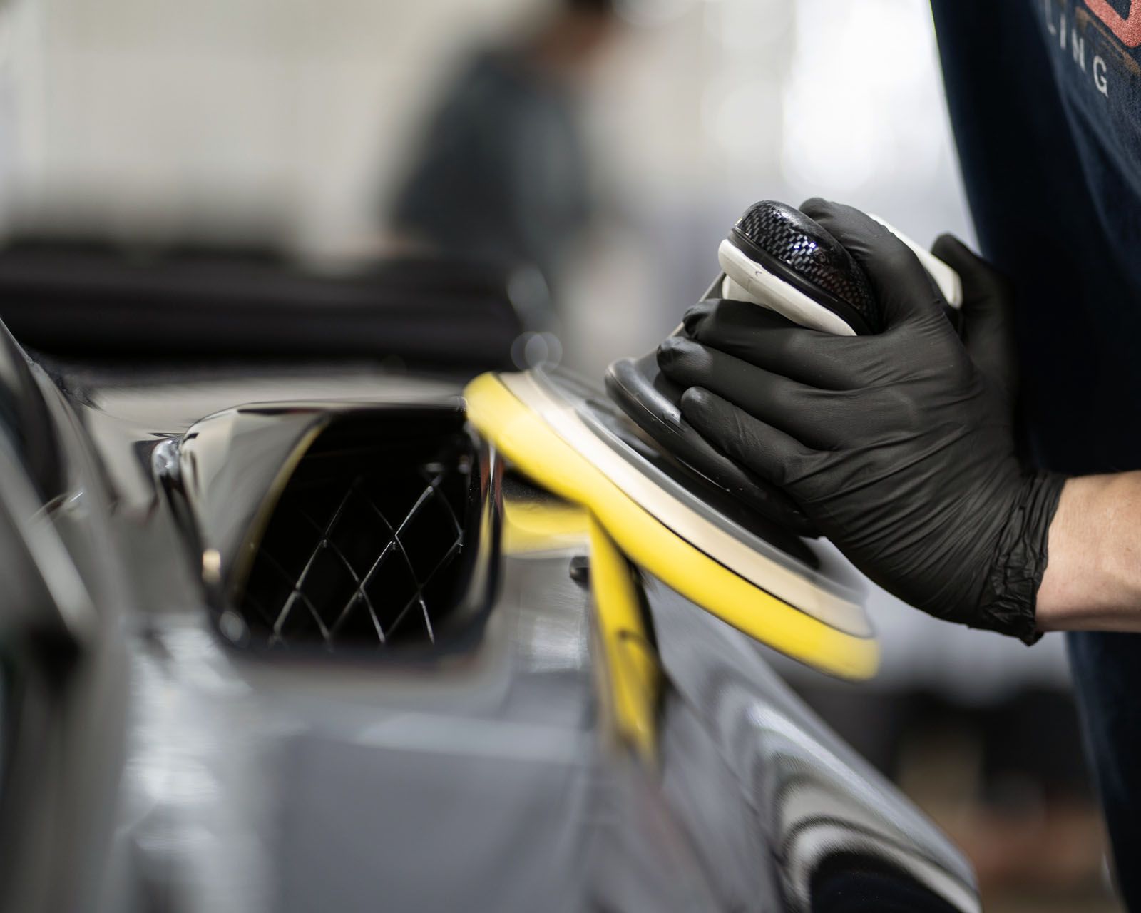 A person wearing black gloves is polishing a car.