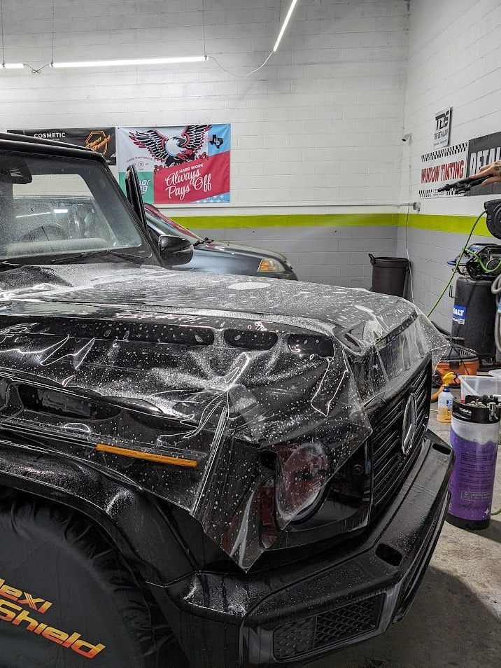 A black jeep is covered in plastic wrap in a garage.