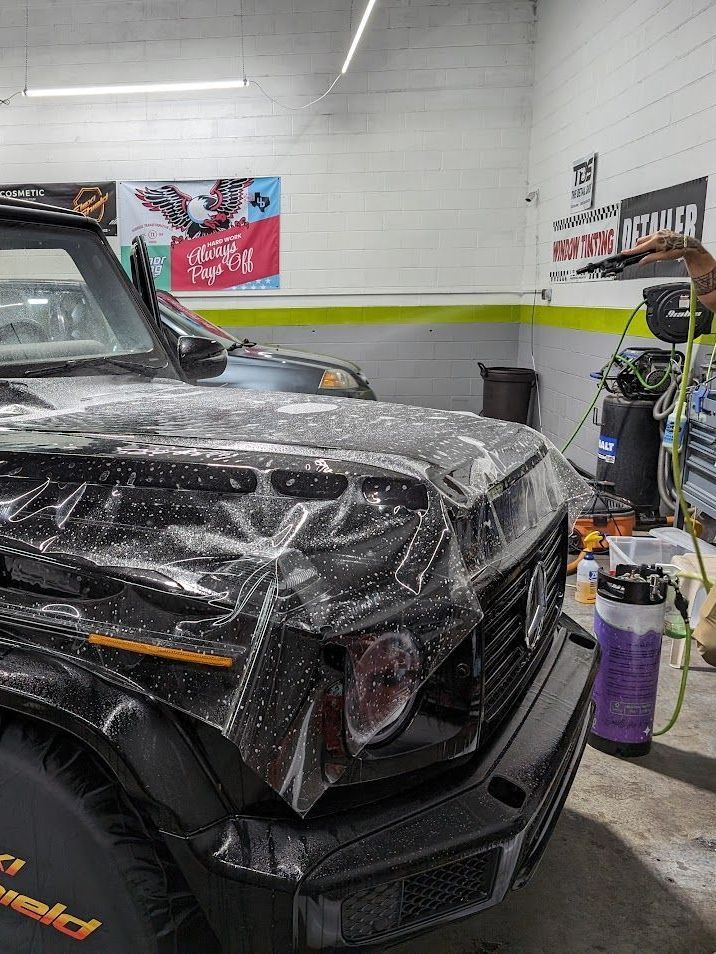 A black jeep is covered in plastic wrap in a garage.