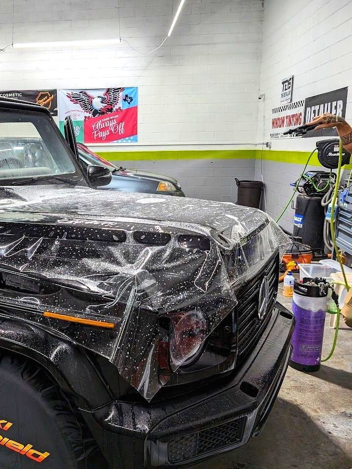 A black jeep is covered in plastic wrap in a garage.