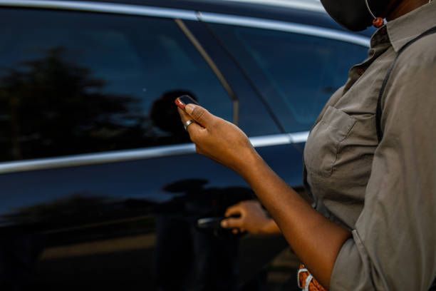 A woman wearing a mask is opening the door of a car.