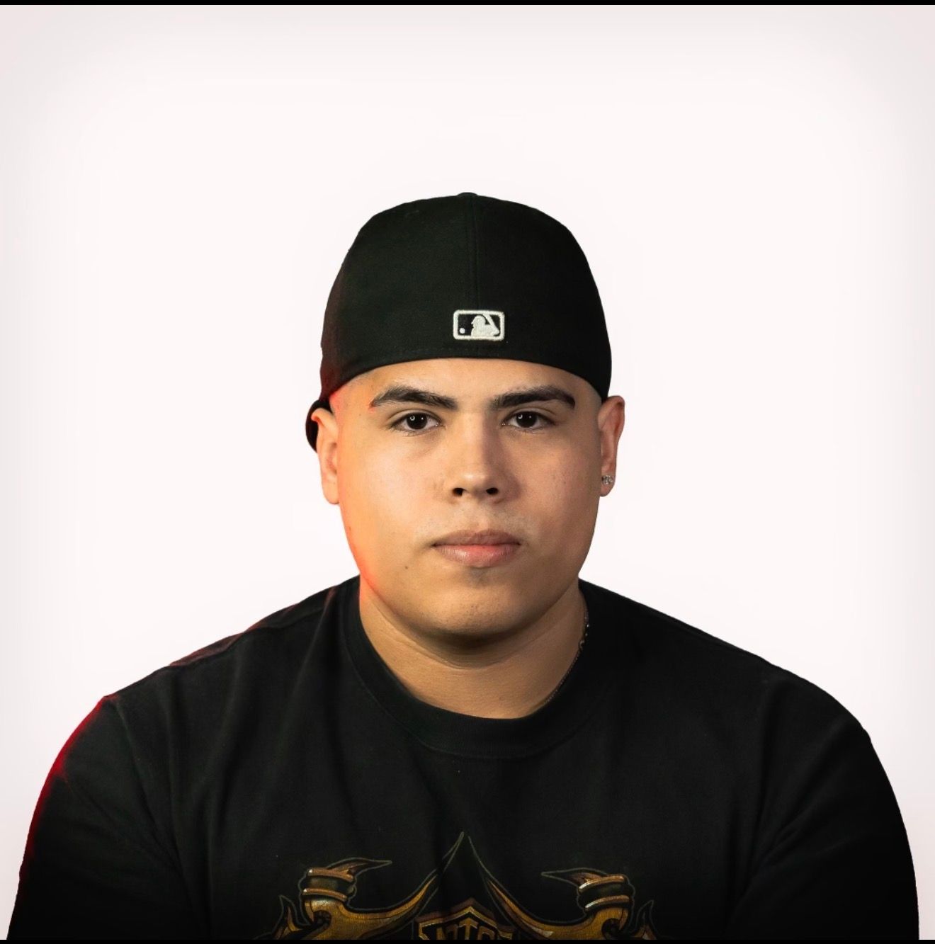 Man in black cap and shirt, looking forward against a white background.
