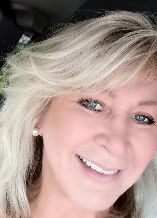 Person working at a light wood desk with a laptop and plants, next to a stool with eucalyptus in a vase.
