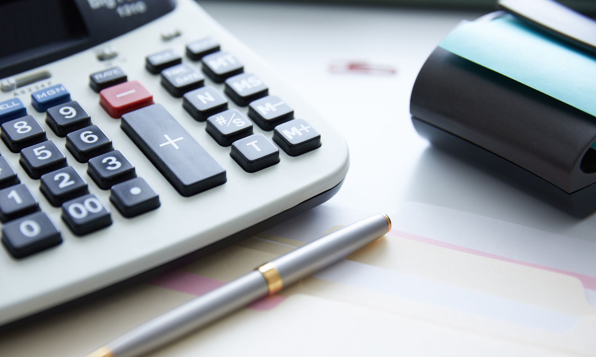 A pen is sitting next to a calculator on a table.