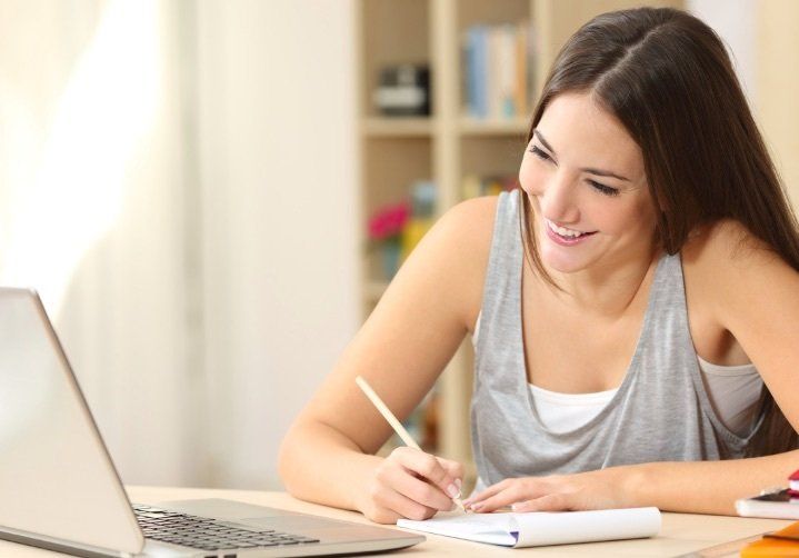 A woman on her laptop, smiling and writing handwritten notes