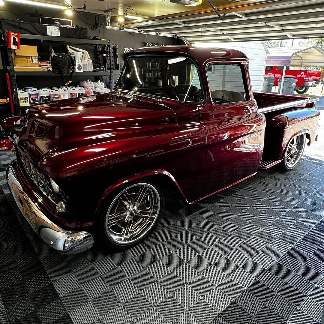 A classic, shiny maroon pickup truck with chrome wheels parked in a garage.
