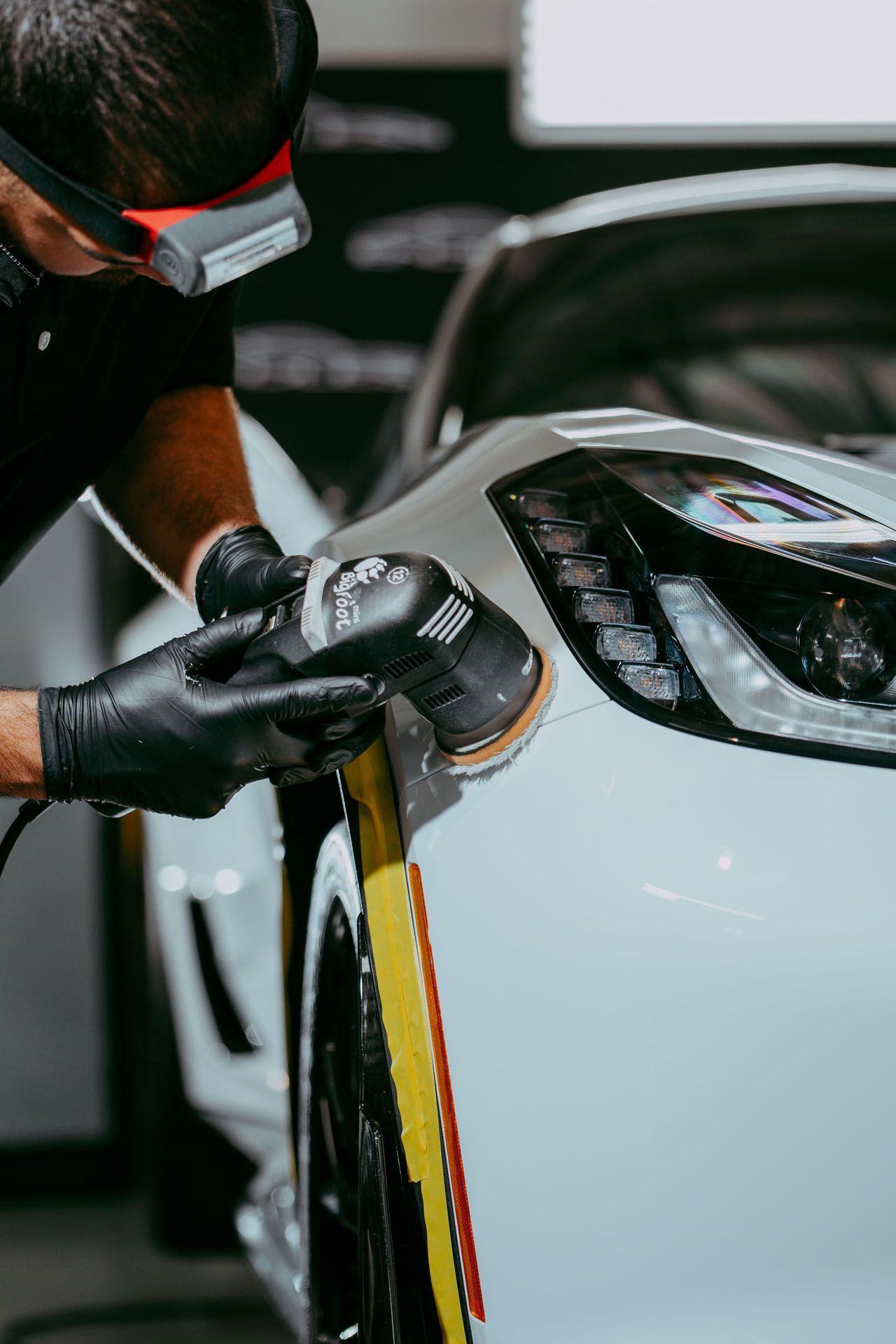 Paint Correction - A man is polishing a white car with a machine.