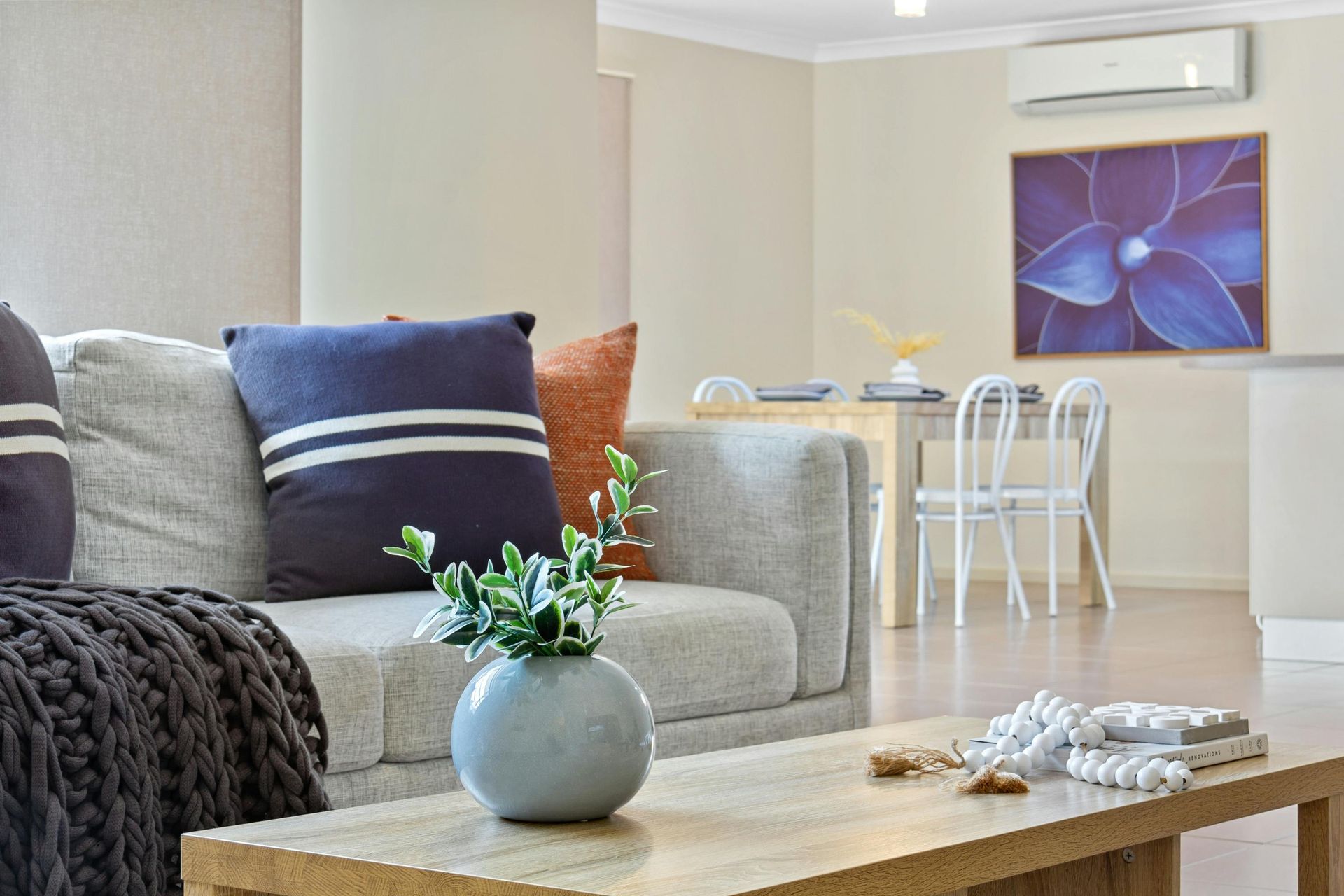 Bright living room with gray sofa, coffee table, dining nook, and purple wall art.