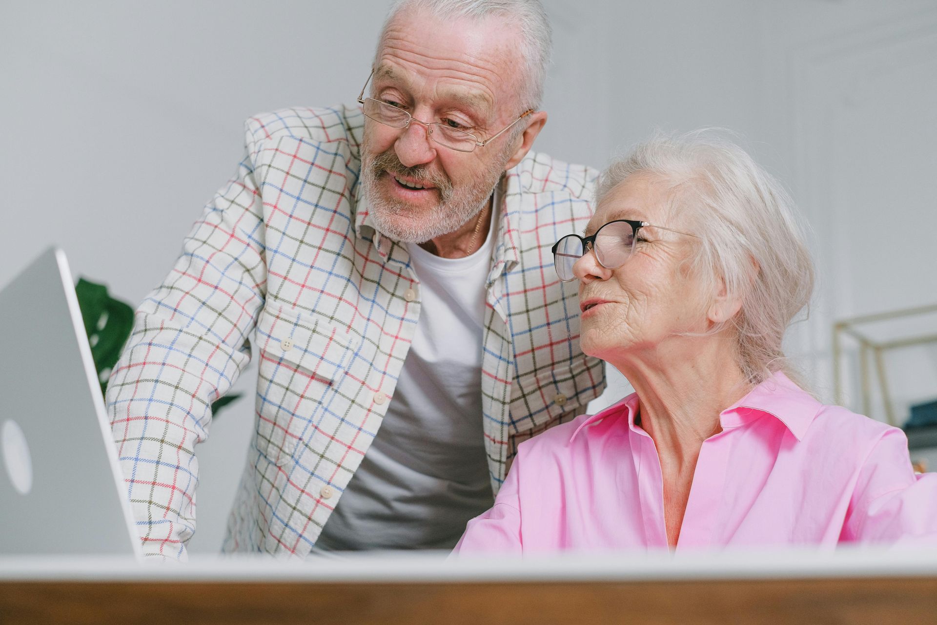 Two older adults smiling while looking at a laptop in a bright room