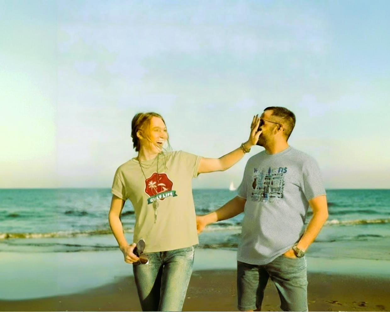 Woman playfully slaps a man's face on a sunny beach.