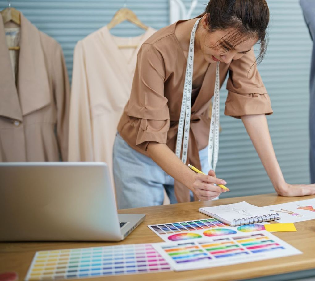 A woman with a measuring tape around her neck is working on a design