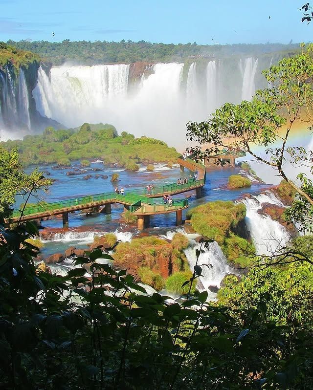 Las imponentes cataratas del Iguazú caen en cascada sobre un río, con un puente peatonal de madera.