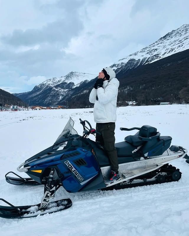 Una persona con una chaqueta acolchada blanca está de pie sobre una moto de nieve Polaris azul.
