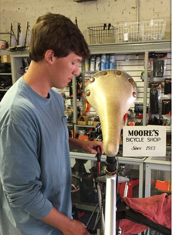 A young man is working on a bicycle in a moore 's bicycle shop