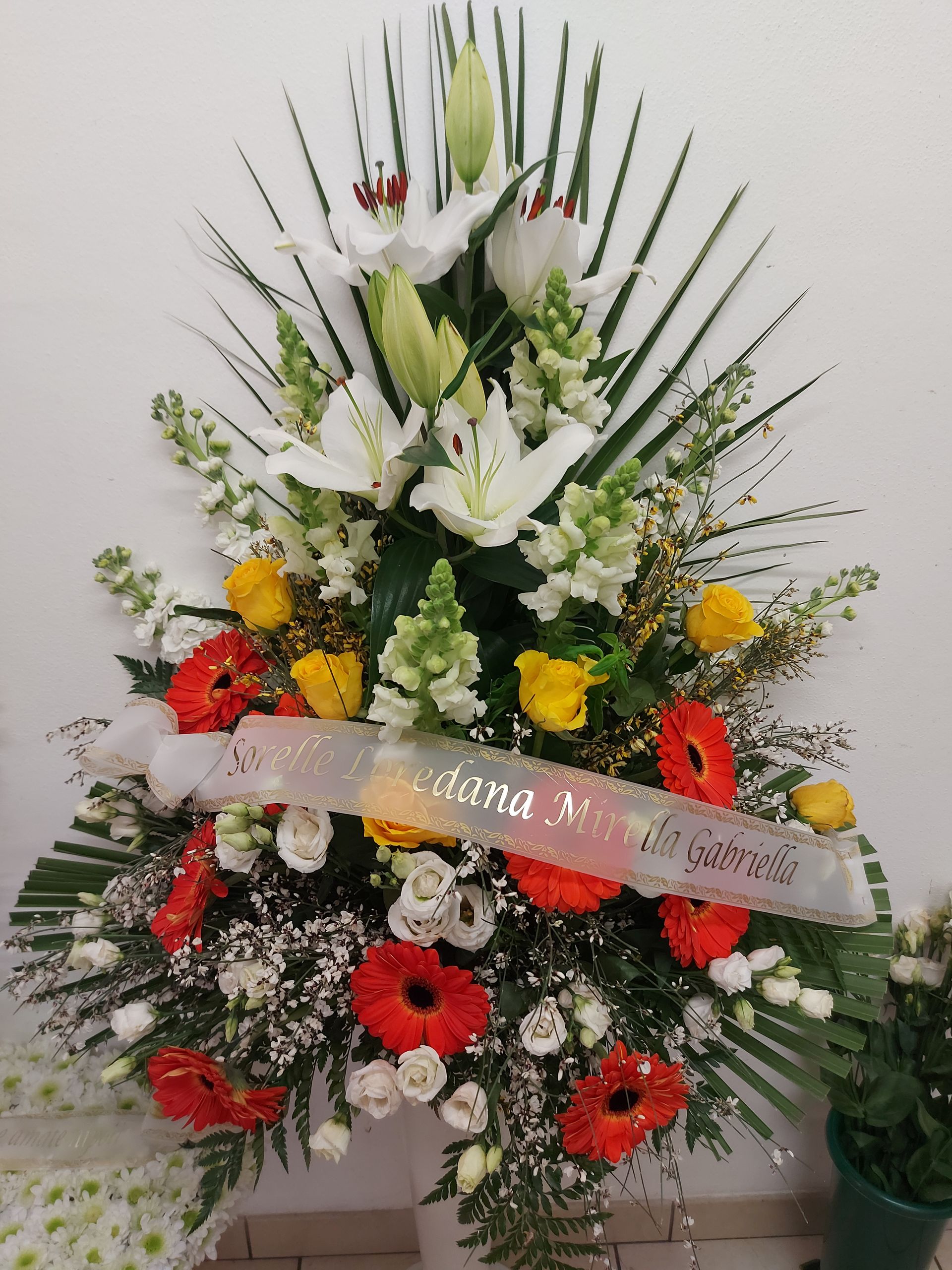 Composizione floreale per funerale, gigli bianchi, gerbere rosse, fiori gialli, verde.