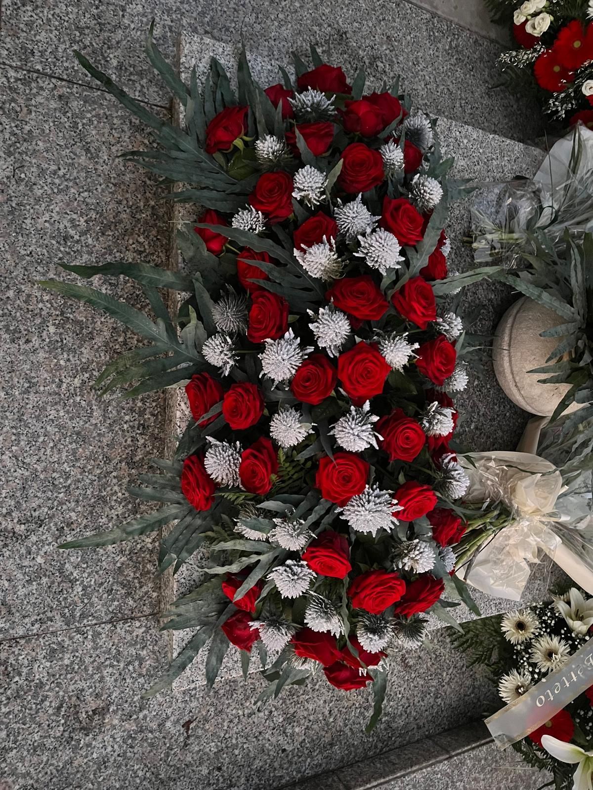 Rose rosse e fiori bianchi in una composizione funebre.