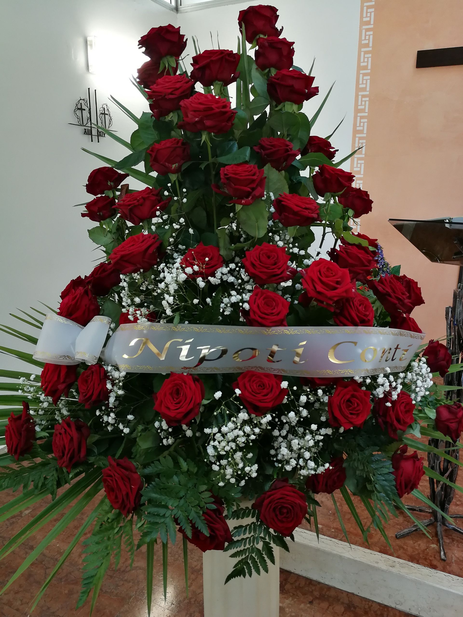 Rose rosse disposte in una composizione floreale con uno striscione bianco con la scritta