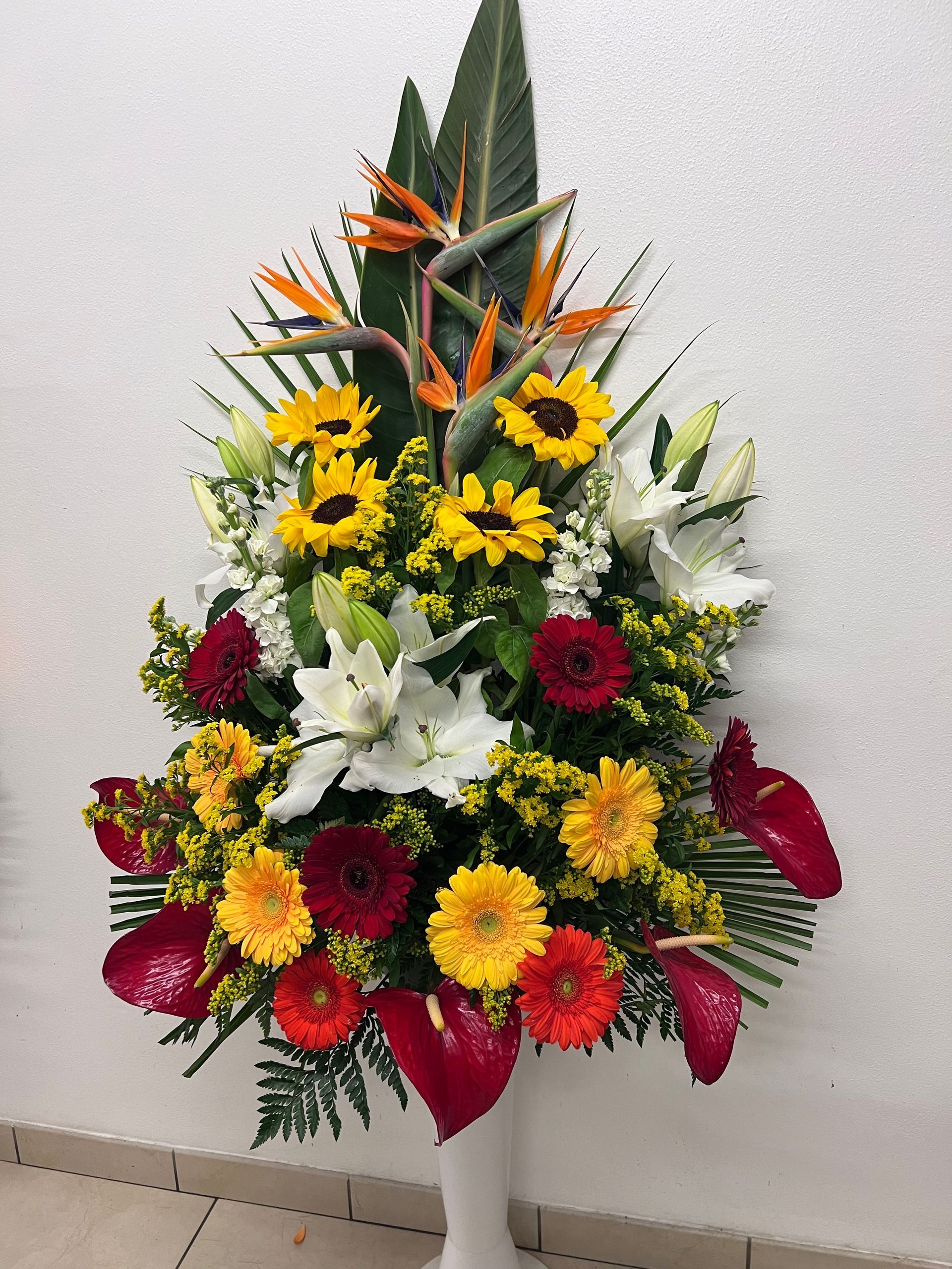 Composizione floreale con girasoli, gigli e strelitzie in un vaso bianco.
