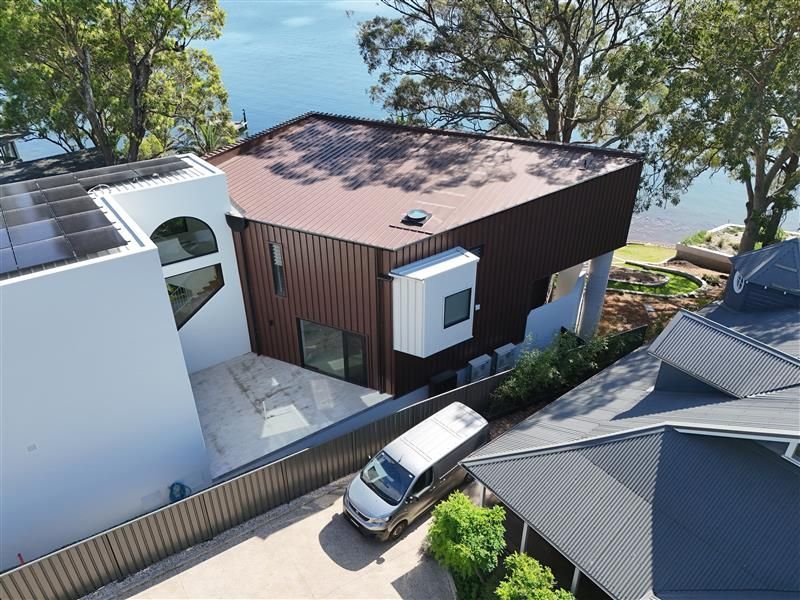 Modern white building with a curved brick base, rooftop access, and black shutter accents.