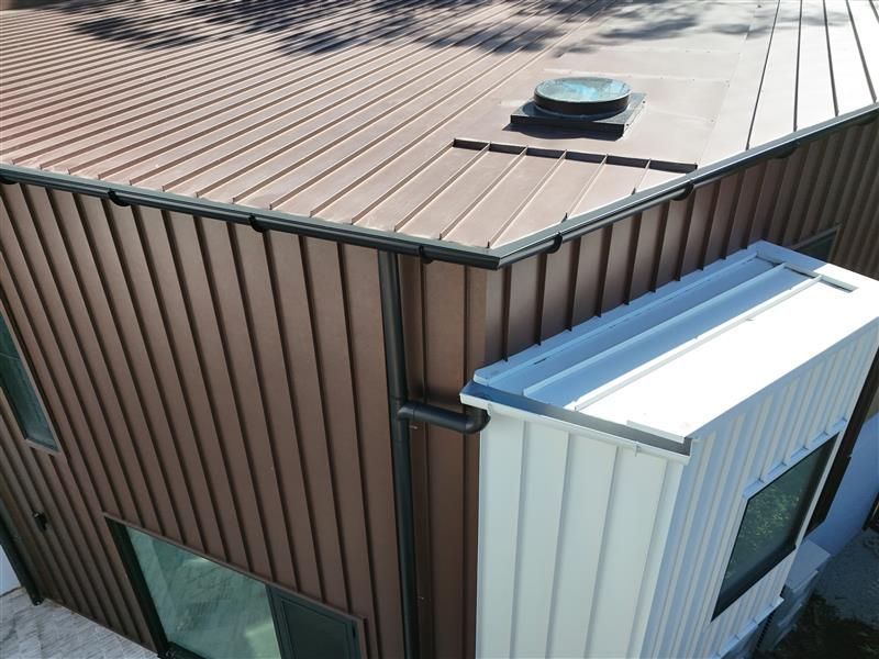 Modern two-story building with dark brick base, white siding, and black trim against a clear blue sky.