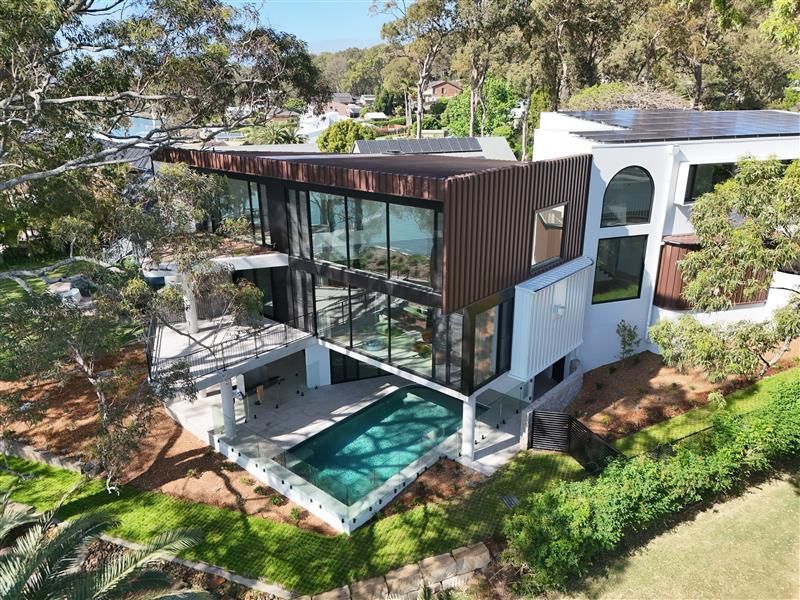 Modern two-story house with white upper level and brick base, dark windows and a blue sky.