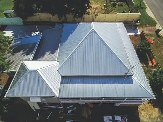 An aerial view of a house with a solar panel on the roof surrounded by trees.
