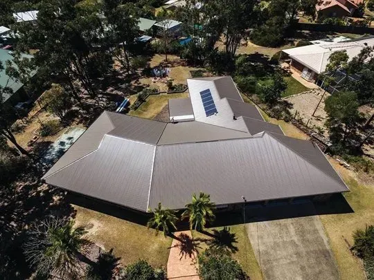 An aerial view of a house with a solar panel on the roof surrounded by trees.