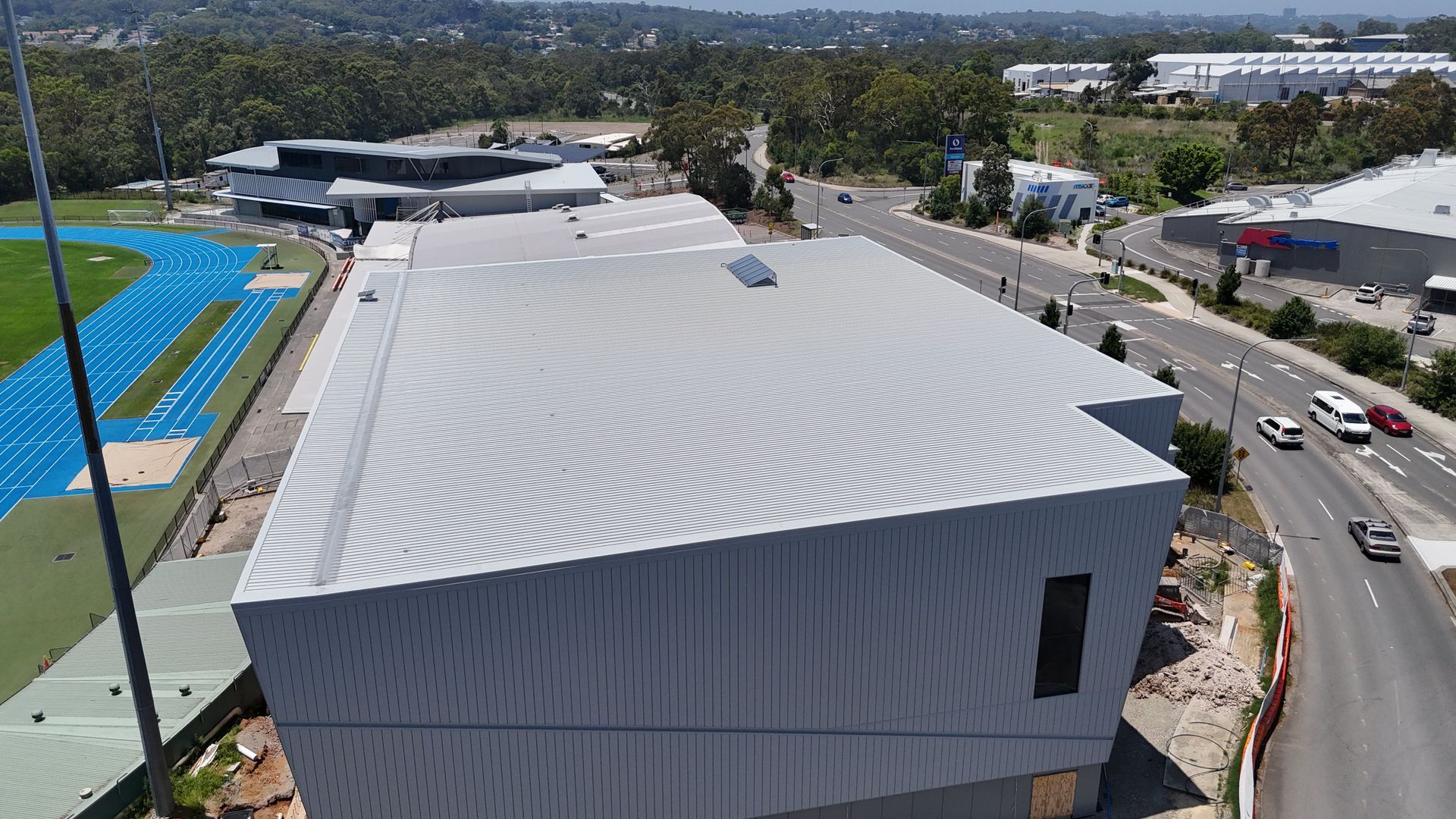 An aerial view of a large building with a white roof and a blue track in the background.