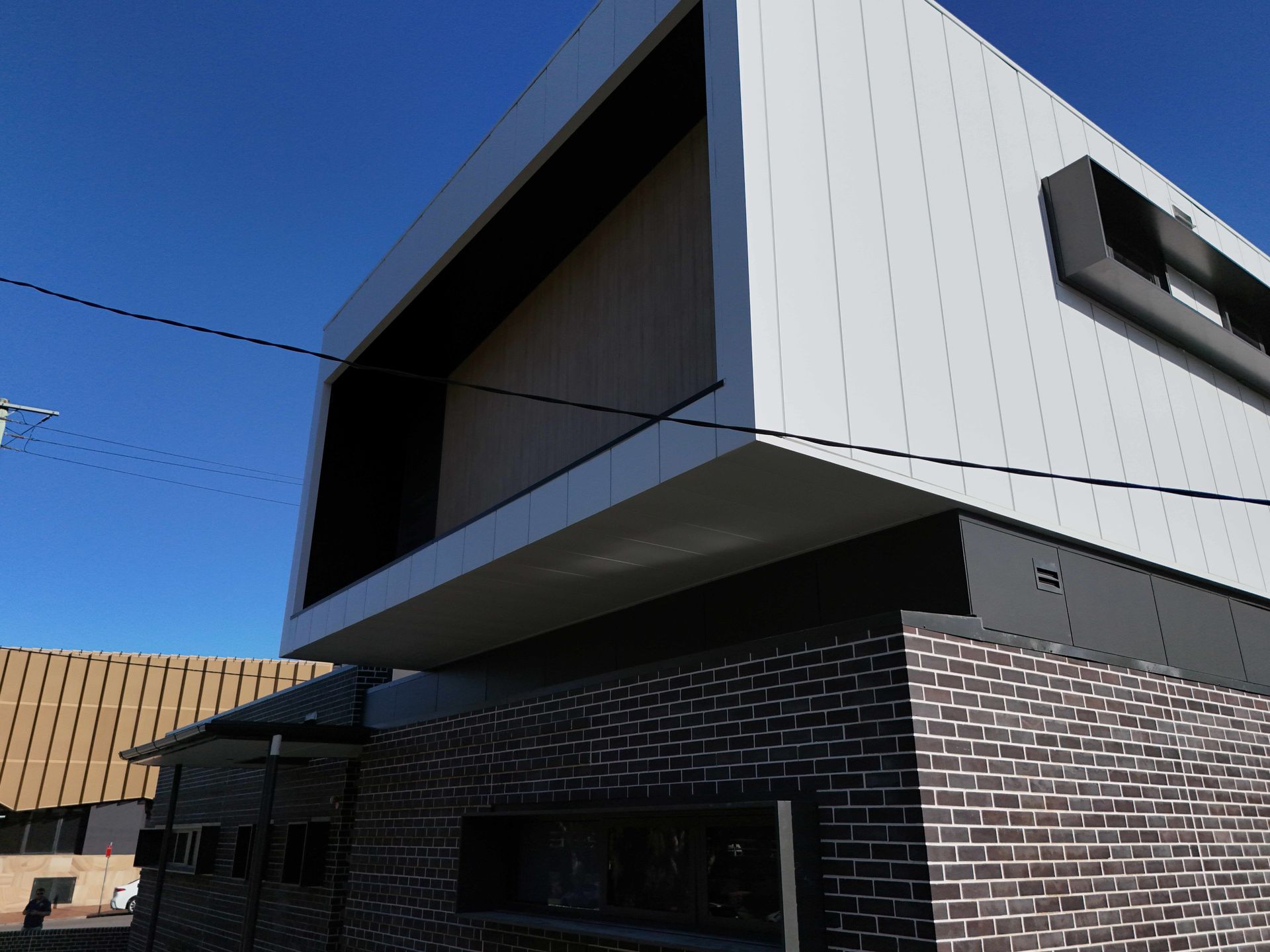 Modern two-story building with dark brick base, white siding, and black trim against a clear blue sky.
