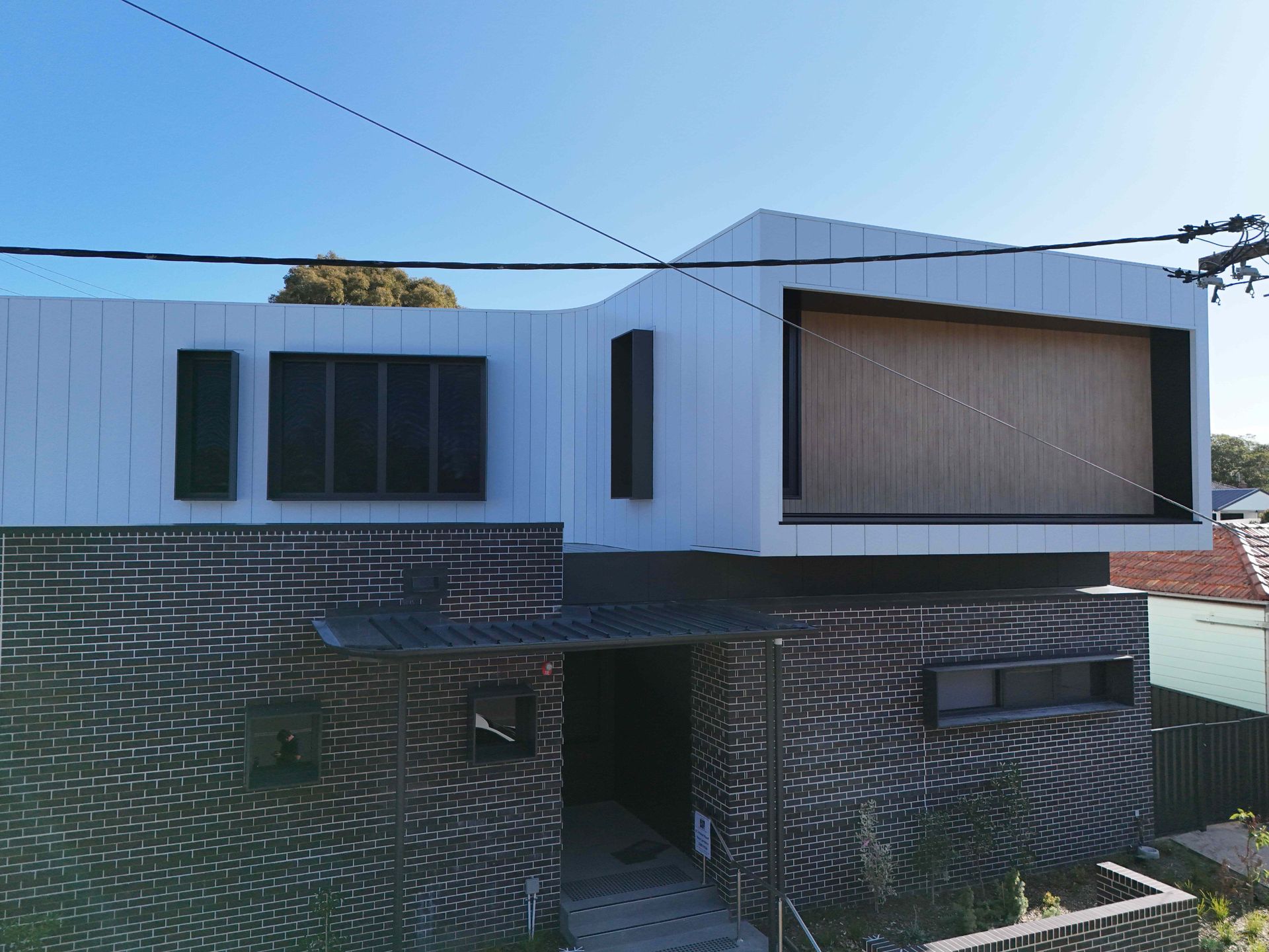 Modern two-story house with white upper level and brick base, dark windows and a blue sky.