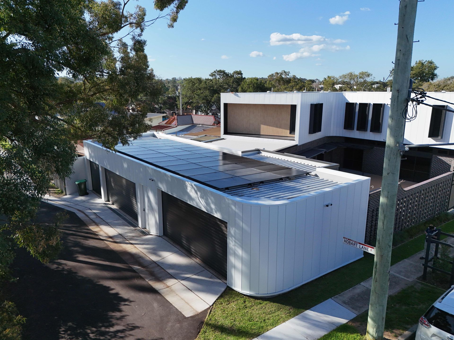 Modern white building with a curved brick base, rooftop access, and black shutter accents.