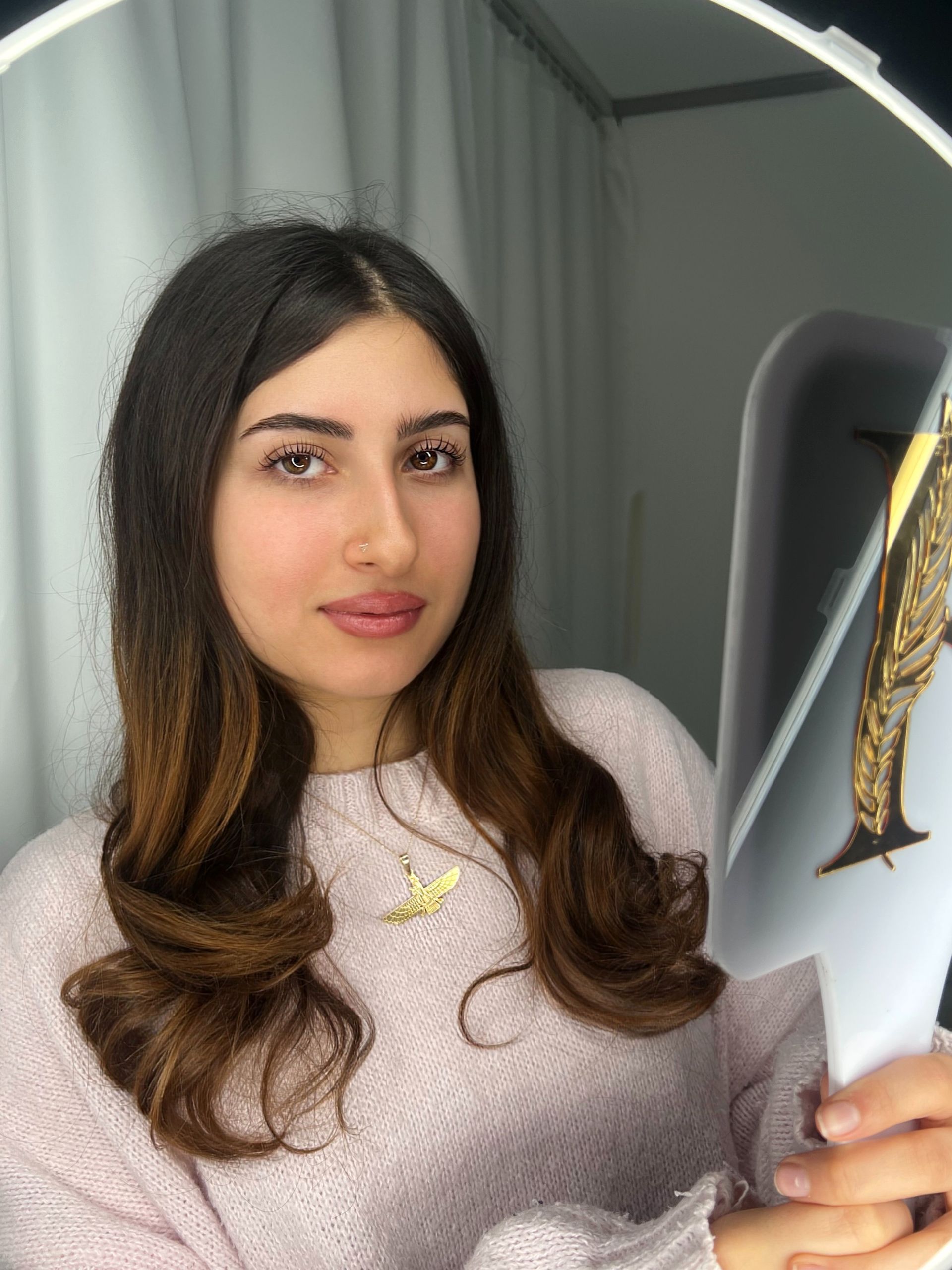 Eine Frau in einem rosa Pullover hält ein Stück Papier vor einen Spiegel.