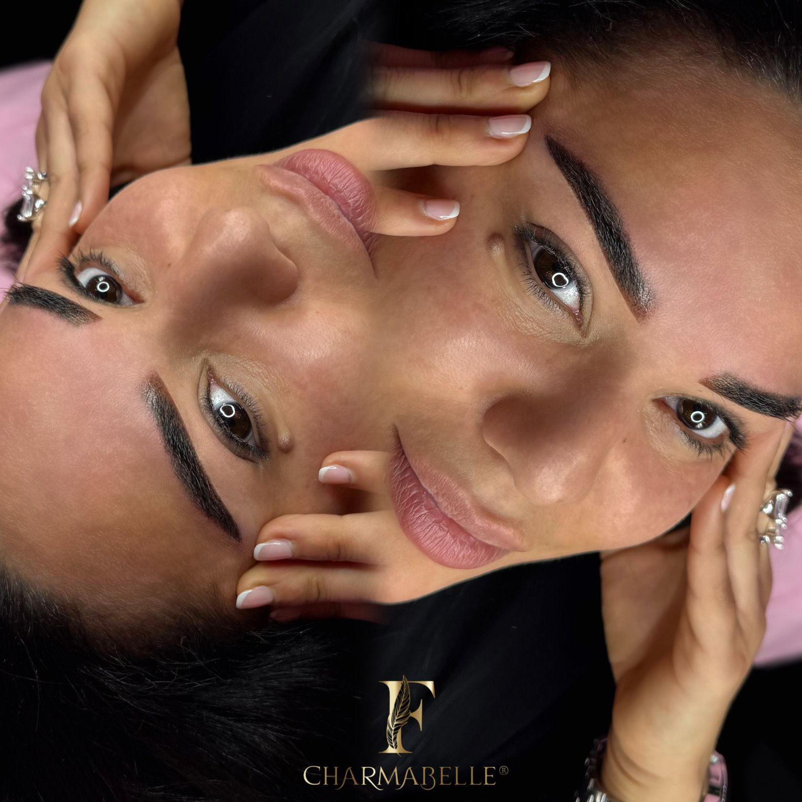 Frau mit Microblading-Augenbrauen, Hände nahe dem Gesicht. Braunes Haar, rosa Hemd, schwarzer Hintergrund.