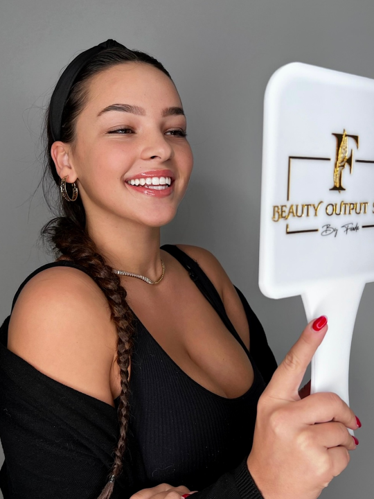 Eine Frau hält einen Handspiegel mit der Aufschrift „Beauty Output“