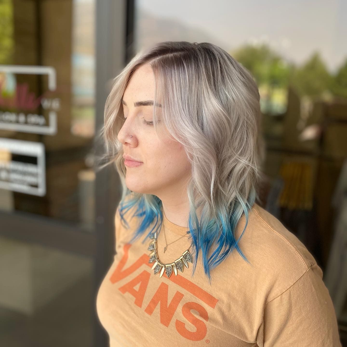 A woman with blue hair is wearing a tan vans shirt.