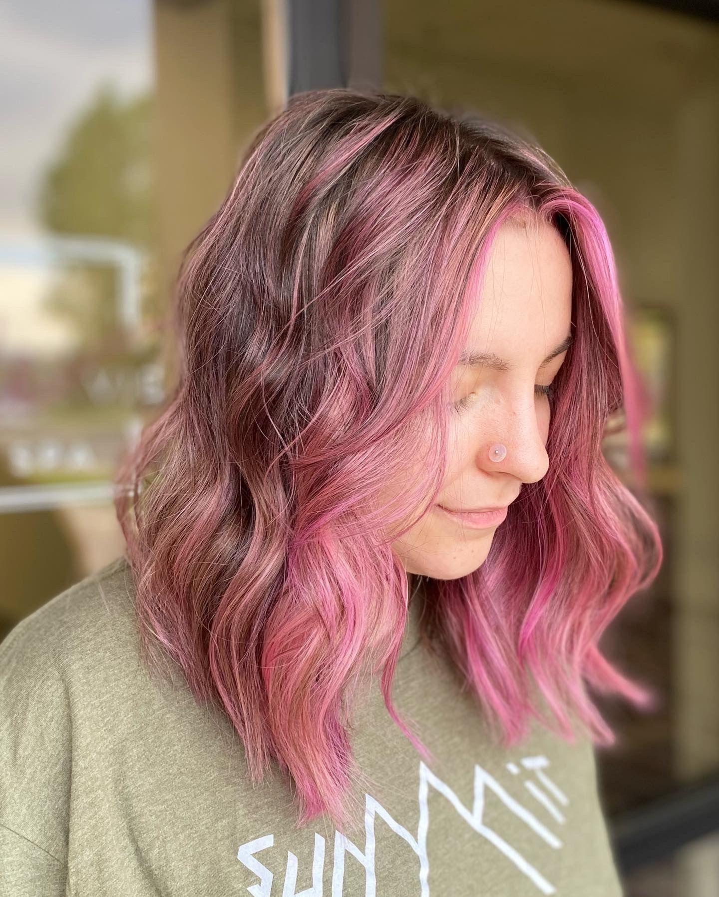 A woman with pink hair is wearing a green shirt.