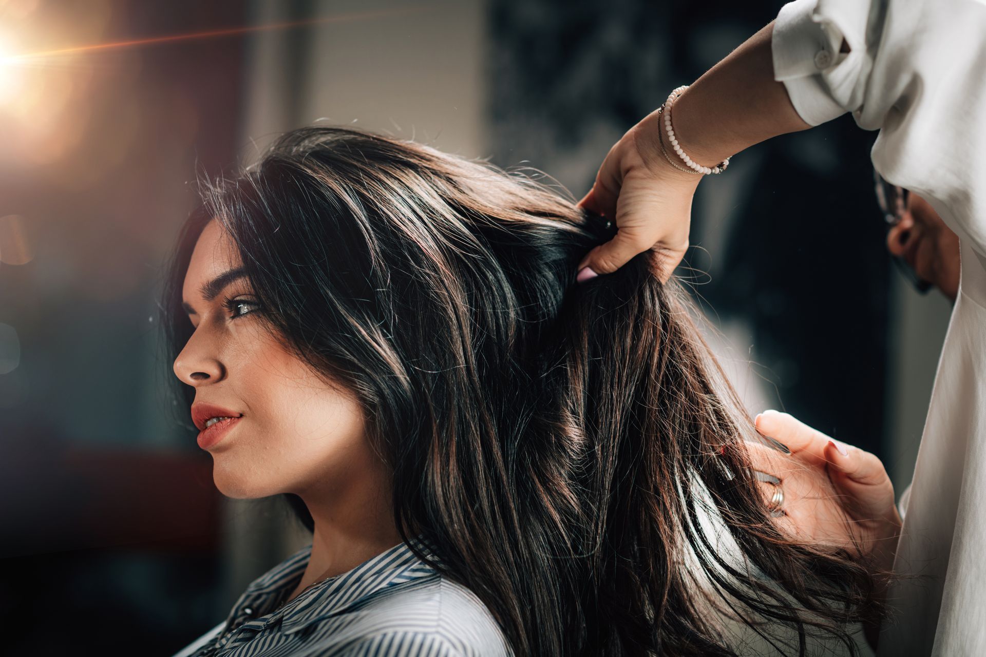 Person getting hair styled at a salon. A stylist's hands in the person's dark hair. Person getting hair styled at a salon. A stylist's hands in the person's dark hair.