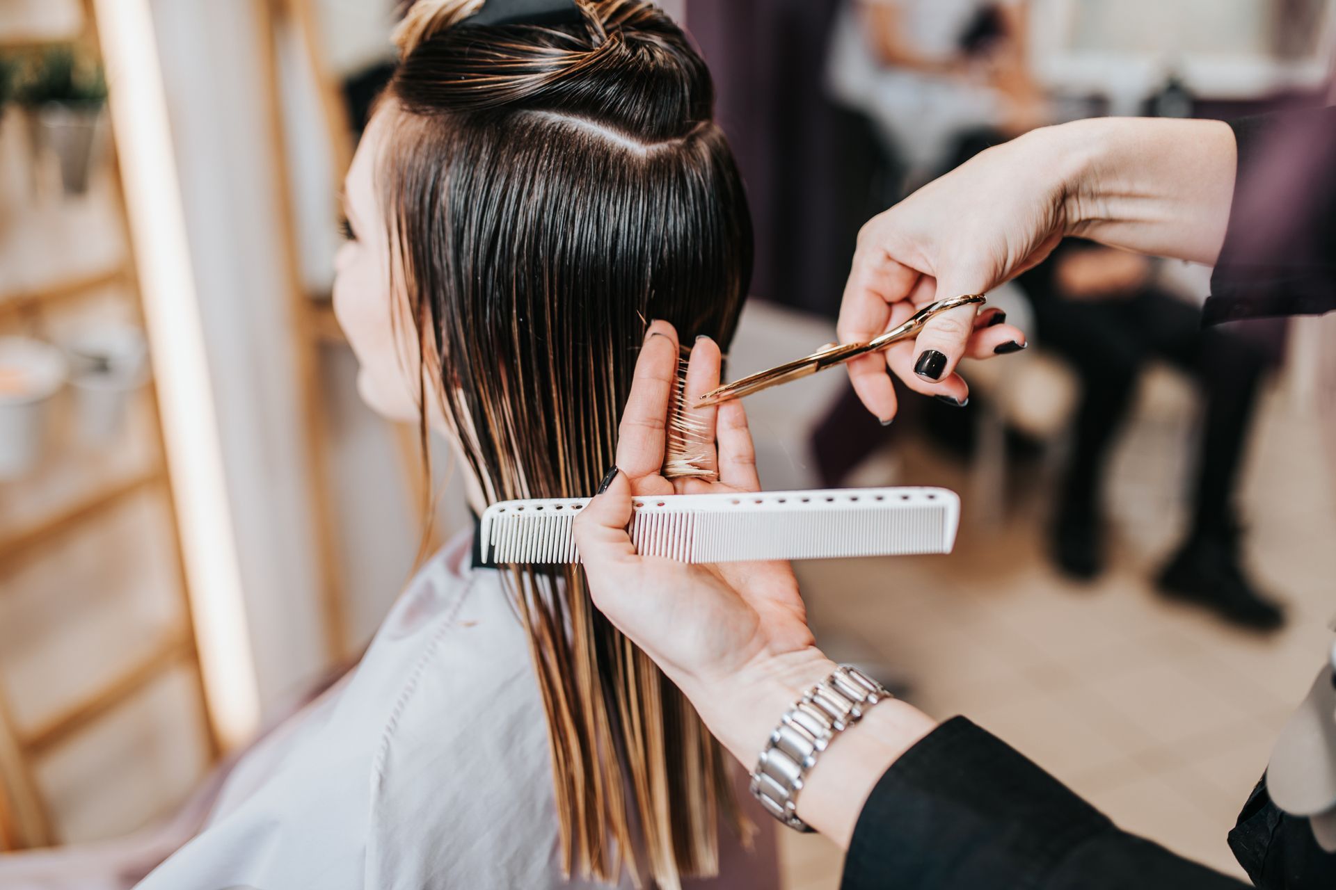Hairdresser cutting a client’s long hair with scissors and a comb in a salon