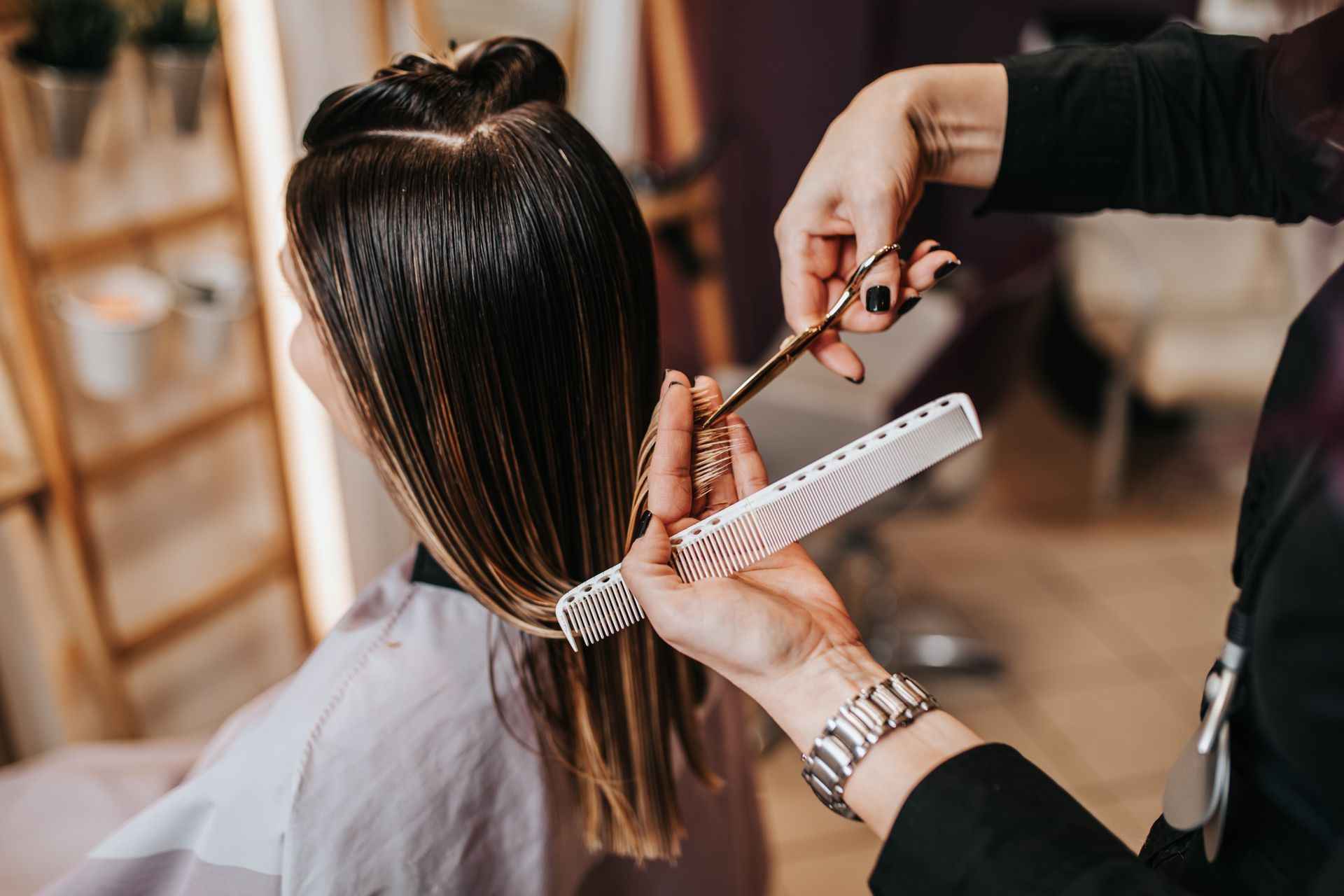 Hairdresser trimming long hair with scissors and a comb during a haircut in a salon setting.