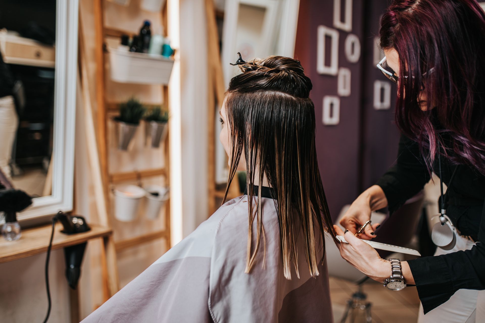 Hairdresser cutting long blonde hair with scissors and comb in a salon