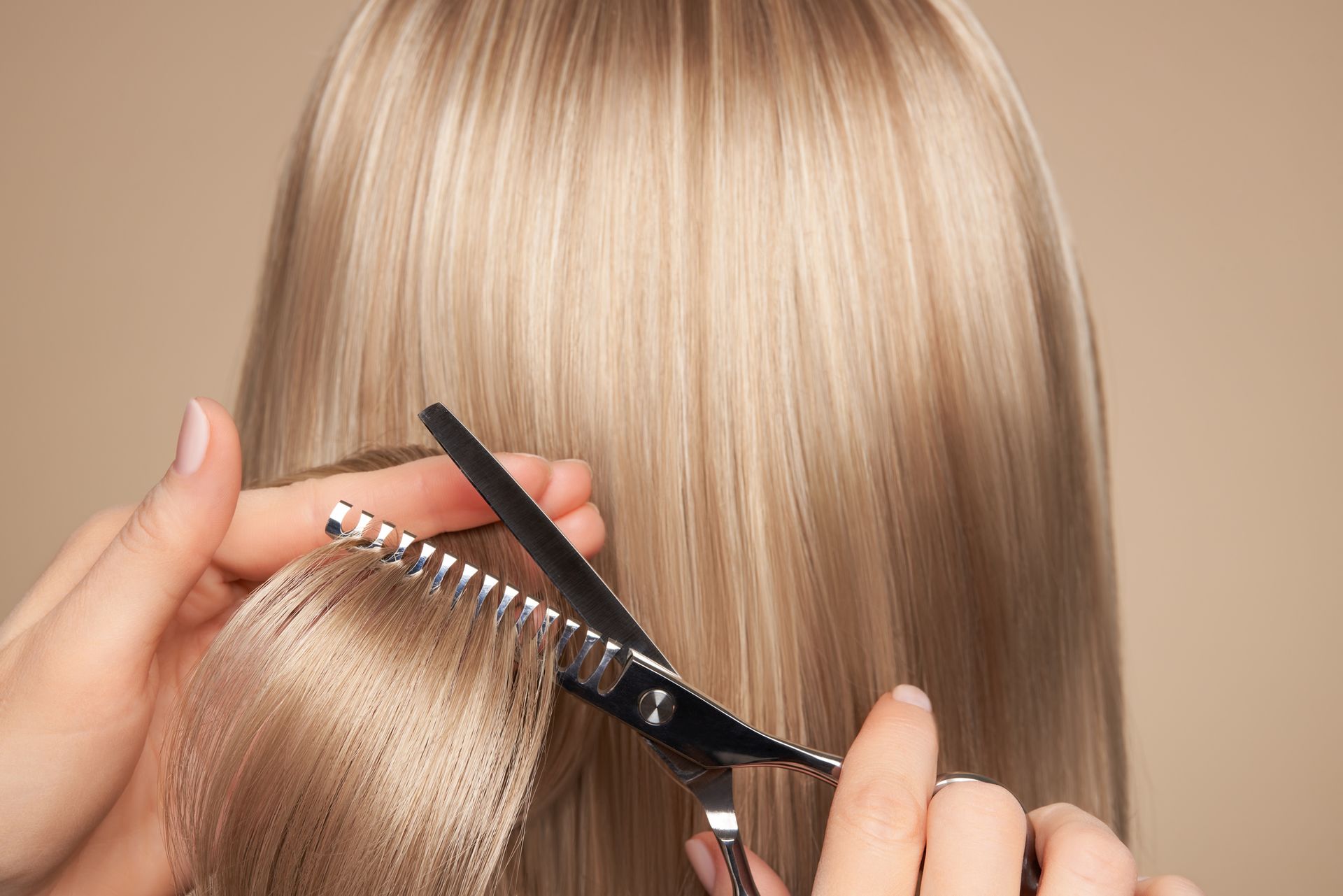 Hairdresser cutting long blonde dyed hair with scissors in a salon setting.