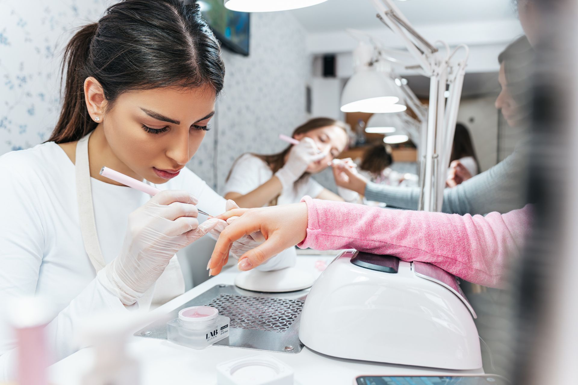 Professional manicurists working in a modern nail salon, and clients receiving manicure treatments. Professional manicurists working in a modern nail salon, and clients receiving manicure treatments.
