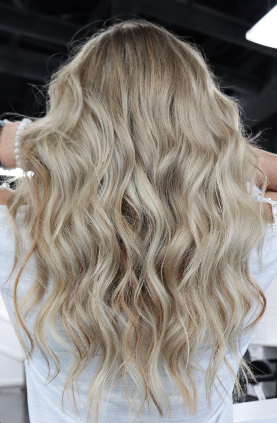 A woman with long blonde wavy hair is wearing a white shirt.