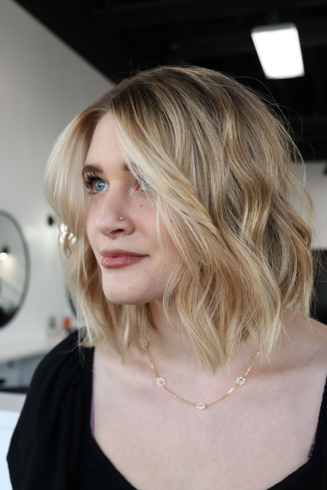 A woman with blonde hair is wearing a black shirt and a gold necklace.