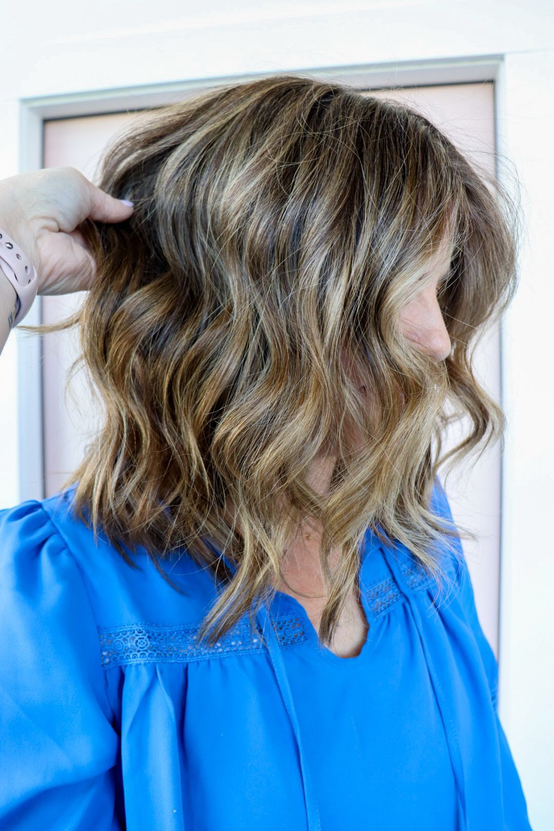 A woman in a blue shirt is touching her hair.