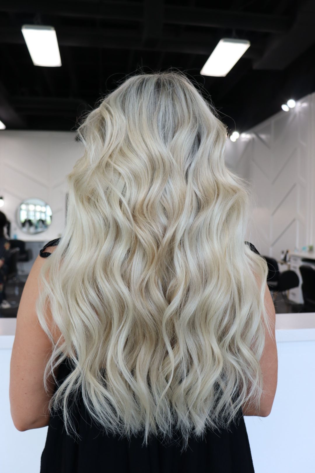 A woman with long blonde wavy hair is standing in a salon.