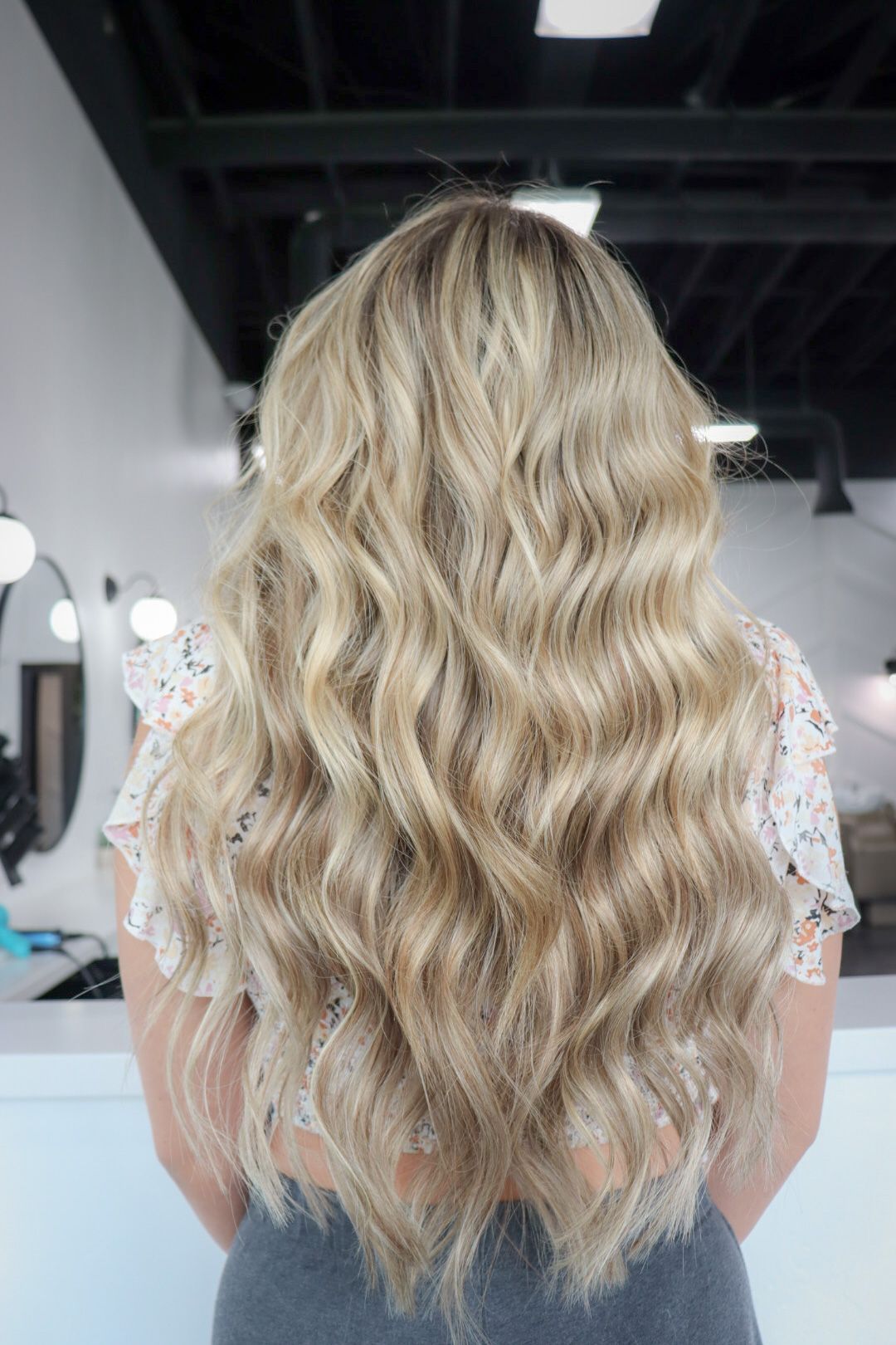 A woman with long blonde wavy hair is standing in a salon.
