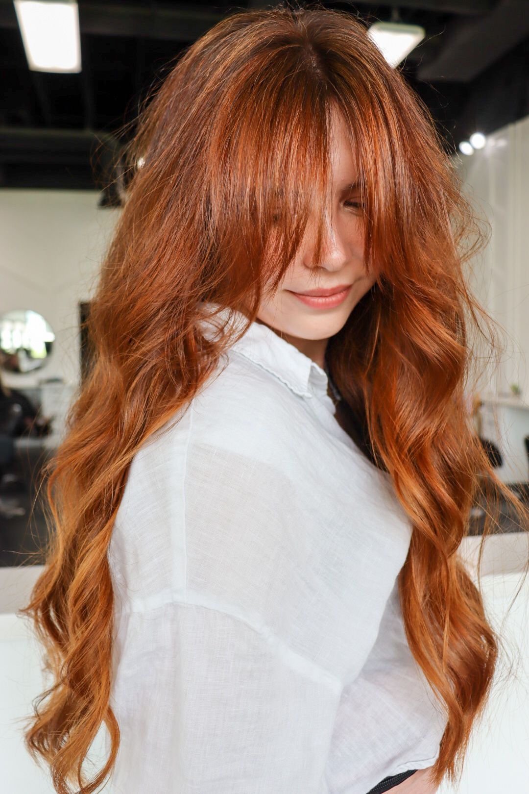A woman with long red hair and bangs is wearing a white shirt.